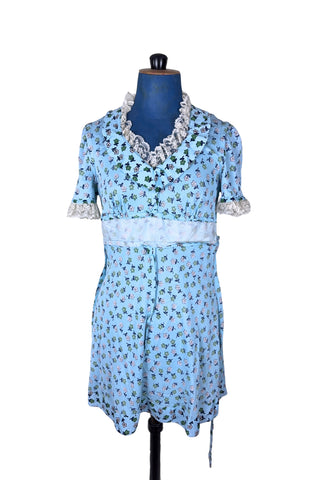 Vintage 1960s mini dress in sky blue with green and white floral print. The V neck and short sleeves are trimmed with wide white lace ruffles. The dress has an inset waistband, with slightly gathered bust. The A-line skirt hits at mid-thigh. The dress closes in the back with a cotton twill zipper and bow sash tie, and is unlined.