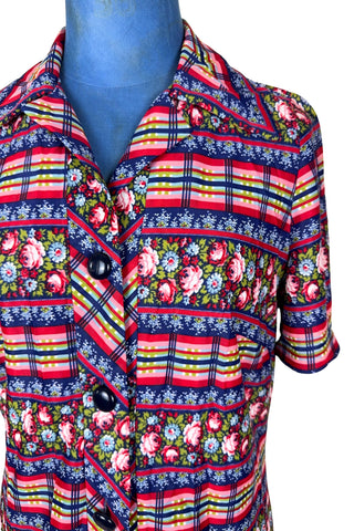 Vintage 1970s day dress with short sleeves and button closure front in a bold blue, yellow, and red ‘crazy’ print with a mixture of floral, stripes and plaid patterns.
The dress closes in the front with four rounded navy lucite buttons, and is unlined.