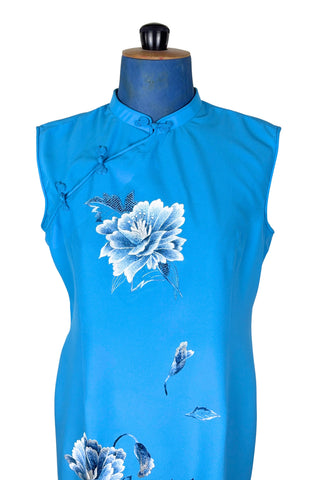 Vintage 1980s cheongsam dress in peacock blue with large white peony flower embroidery. The dress is sleeveless, with a mandarin collar, and closes with three frog closures across the chest, and a side zipper. The dress is unlined.