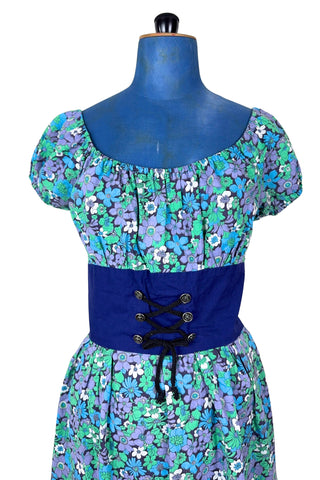 Vintage 1960s mini dress with laced bodice inspired by Alpine dirndl. The dress features a wide gathered neckline and puff sleeves, and closes in the back with a cotton twill zipper. It is made from green and blue floral print cotton with a wide navy blue bodice with silver crest buttons. The dress is unlined.