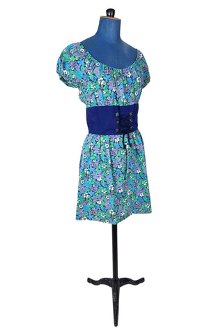 Vintage 1960s mini dress with laced bodice inspired by Alpine dirndl. The dress features a wide gathered neckline and puff sleeves, and closes in the back with a cotton twill zipper. It is made from green and blue floral print cotton with a wide navy blue bodice with silver crest buttons. The dress is unlined.