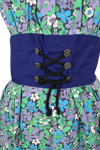 Vintage 1960s mini dress with laced bodice inspired by Alpine dirndl. The dress features a wide gathered neckline and puff sleeves, and closes in the back with a cotton twill zipper. It is made from green and blue floral print cotton with a wide navy blue bodice with silver crest buttons. The dress is unlined.