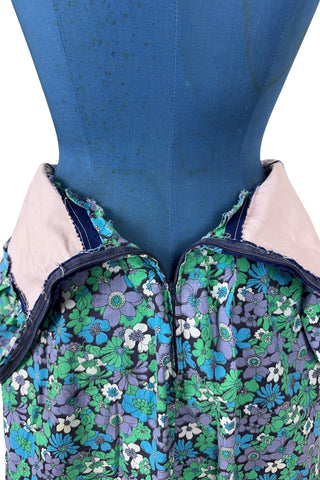 Vintage 1960s mini dress with laced bodice inspired by Alpine dirndl. The dress features a wide gathered neckline and puff sleeves, and closes in the back with a cotton twill zipper. It is made from green and blue floral print cotton with a wide navy blue bodice with silver crest buttons. The dress is unlined.
