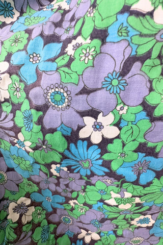 Vintage 1960s mini dress with laced bodice inspired by Alpine dirndl. The dress features a wide gathered neckline and puff sleeves, and closes in the back with a cotton twill zipper. It is made from green and blue floral print cotton with a wide navy blue bodice with silver crest buttons. The dress is unlined.