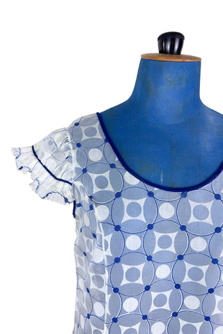 Vintage 1960s babydoll nightie in white and navy blue geometric ‘flowering snowball’ pattern. The white and blue pattern is printed onto sheer white chiffon, creating a 3D effect. The nightie has a wide round collar finished with navy blue piping, which is echoed at the hem and along the edges of the cap sleeves. The hem and sleeves are trimmed with delicate accordion pleated frills.