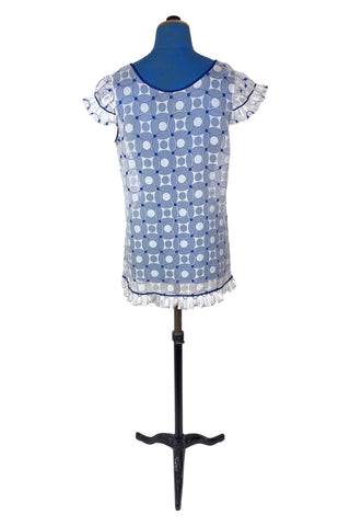 Vintage 1960s babydoll nightie in white and navy blue geometric ‘flowering snowball’ pattern. The white and blue pattern is printed onto sheer white chiffon, creating a 3D effect. The nightie has a wide round collar finished with navy blue piping, which is echoed at the hem and along the edges of the cap sleeves. The hem and sleeves are trimmed with delicate accordion pleated frills.