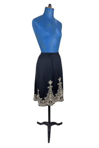 Vintage 1950s half slip in black with intricate cream corded lace decoration at the hem. The waist is elasticized.