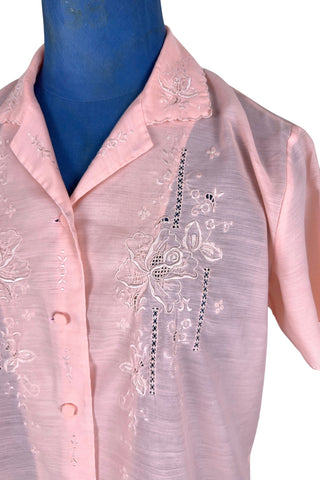 Vintage 1970s pink blouse with floral embroidery and covered buttons. Features short sleeves with scalloped edges, and an embroidered pointed collar.