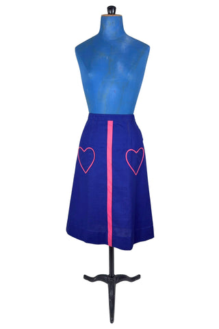 Vintage 1970s A-line skirt in navy blue cotton with pink heart shaped pockets and stripe down the front. Closes in the left side with four hook and eye closures.