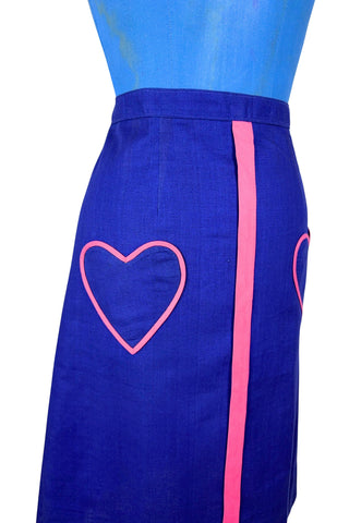 Vintage 1970s A-line skirt in navy blue cotton with pink heart shaped pockets and stripe down the front. Closes in the left side with four hook and eye closures.