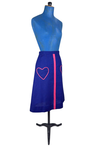 Vintage 1970s A-line skirt in navy blue cotton with pink heart shaped pockets and stripe down the front. Closes in the left side with four hook and eye closures.