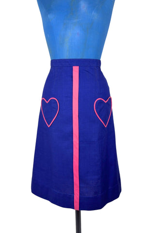 Vintage 1970s A-line skirt in navy blue cotton with pink heart shaped pockets and stripe down the front. Closes in the left side with four hook and eye closures.
