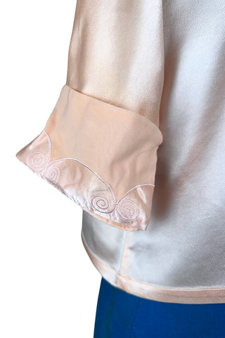 Vintage 1930s silk bed jacket with mandarin collar in mixed satin and crepe silk, with embroidered appliqué flowers and swirls. The three-quarter length sleeves have wide folded cuffs embellished with matching embroidered swirls. Closes in the front with three sets of tiny shiny buttons that resemble ivory.

Label reads Classic Silk Underwear. Made in Canada. Size Small.