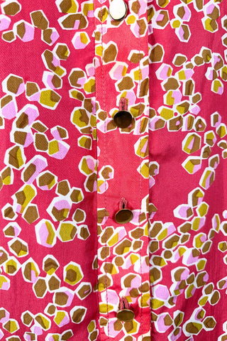 Vintage 1970s silk day dress in abstract ‘pebble’ print in shades of brown and pink on a pinkish red background. The dress has short sleeves, a wide pointed collar, and closes down the front with six flat gold metal buttons.
