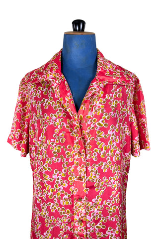 Vintage 1970s silk day dress in abstract ‘pebble’ print in shades of brown and pink on a pinkish red background. The dress has short sleeves, a wide pointed collar, and closes down the front with six flat gold metal buttons.