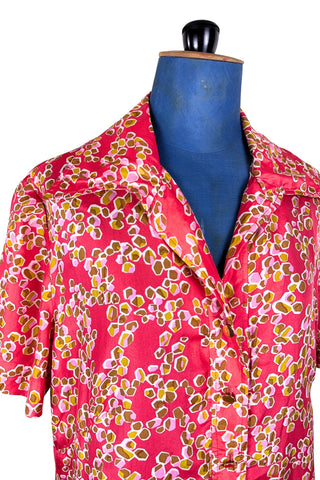 Vintage 1970s silk day dress in abstract ‘pebble’ print in shades of brown and pink on a pinkish red background. The dress has short sleeves, a wide pointed collar, and closes down the front with six flat gold metal buttons.