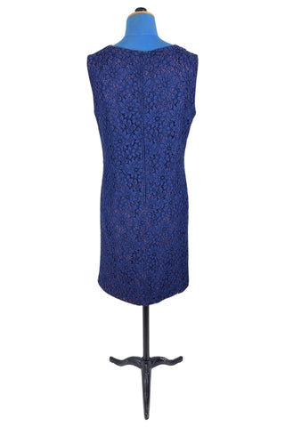 Vintage 1950s cocktail dress in navy blue floral lace, featuring open corded lace over a contrasting mauve lining. The sleeveless sheath dress has a boatneck neckline trimmed with navy cord which is gathered into a flower brooch. The dress closes in the back with a cotton twill zipper.