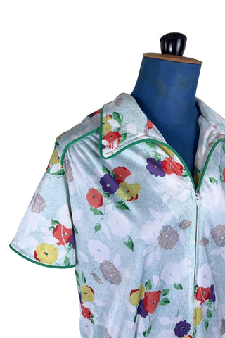 Vintage 1970s house dress in sky blue nylon jersey with a multicolour floral pansy print in red, yellow, purple, and white. The short sleeves and pointed collar are trimmed with grass green piping. Closes with a zipper down the front.

Designed by Windsor.