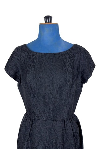 The perfect vintage 1950s little black dress. Perfect for either day or evening wear, with a classic hourglass silhouette and simple round collar and short sleeve sheath design. The skirt is gathered gently into the waist at the hips. The waist is accentuated with matching piping. The dress closes in the back with a metal zipper, and is unlined.

Designed by Roma. Union made by ILGWU AFL-CIO.