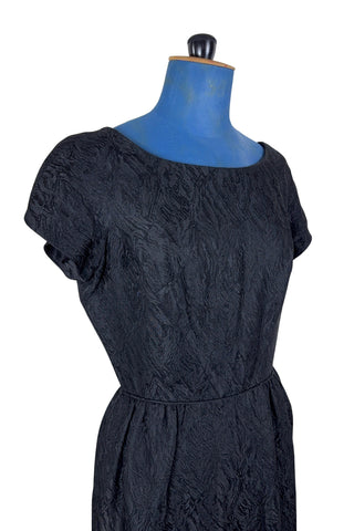 The perfect vintage 1950s little black dress. Perfect for either day or evening wear, with a classic hourglass silhouette and simple round collar and short sleeve sheath design. The skirt is gathered gently into the waist at the hips. The waist is accentuated with matching piping. The dress closes in the back with a metal zipper, and is unlined.

Designed by Roma. Union made by ILGWU AFL-CIO.