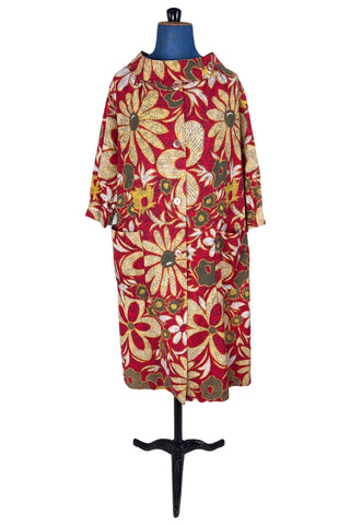 Vintage 1960s cotton robe with giant yellow and beige floral print on a red background. The housecoat features a wide standing collar, three quarter sleeves with slightly gathered buttoned cuffs, and large square pockets. Closes with five pearly buttons down the front, and one at the side of the collar.