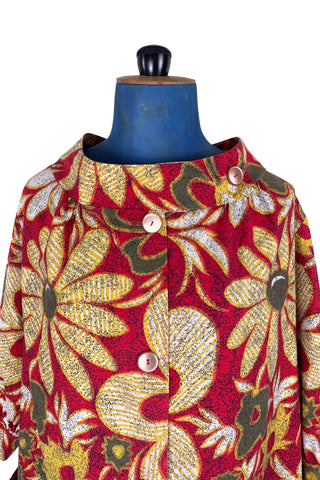 Vintage 1960s cotton robe with giant yellow and beige floral print on a red background. The housecoat features a wide standing collar, three quarter sleeves with slightly gathered buttoned cuffs, and large square pockets. Closes with five pearly buttons down the front, and one at the side of the collar.