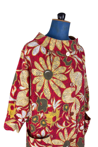 Vintage 1960s cotton robe with giant yellow and beige floral print on a red background. The housecoat features a wide standing collar, three quarter sleeves with slightly gathered buttoned cuffs, and large square pockets. Closes with five pearly buttons down the front, and one at the side of the collar.
