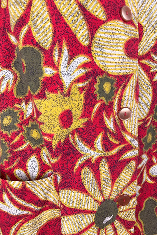 Vintage 1960s cotton robe with giant yellow and beige floral print on a red background. The housecoat features a wide standing collar, three quarter sleeves with slightly gathered buttoned cuffs, and large square pockets. Closes with five pearly buttons down the front, and one at the side of the collar.
