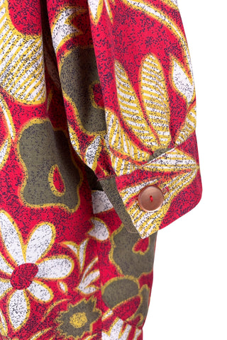 Vintage 1960s cotton robe with giant yellow and beige floral print on a red background. The housecoat features a wide standing collar, three quarter sleeves with slightly gathered buttoned cuffs, and large square pockets. Closes with five pearly buttons down the front, and one at the side of the collar.