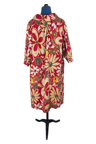 Vintage 1960s cotton robe with giant yellow and beige floral print on a red background. The housecoat features a wide standing collar, three quarter sleeves with slightly gathered buttoned cuffs, and large square pockets. Closes with five pearly buttons down the front, and one at the side of the collar.
