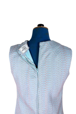 Simple and elegant vintage 1960s shift dress in light blue with a raised silver textured geometric pattern resembling fish or lizard scales. The sleeveless dress features a round collar and darts at the bust to add shape. The dress closes in the back with a cotton twill zipper, and is unlined.

This dress was made from a Vogue pattern, which would have included a Vogue Couturier Design label in the pattern package, intended to be added to the garment after sewing it from the pattern at home.