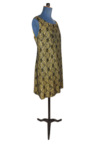 Vintage 1960s cocktail dress with sheer black lace layered over a bright yellow lining. The dress is sleeveless, with straps that narrow towards the back, and a wide, round neckline. Closes in the back with a cotton twill zipper.