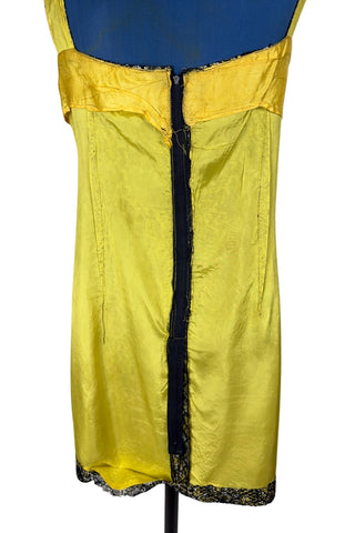 Vintage 1960s cocktail dress with sheer black lace layered over a bright yellow lining. The dress is sleeveless, with straps that narrow towards the back, and a wide, round neckline. Closes in the back with a cotton twill zipper.