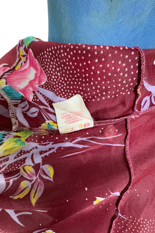 Vintage 1970s dress in burgundy red with a tulip and dianthus floral print. Features short flutter sleeves and a round neckline that can be gathered with the bow tie. The bodice closes with three white diamond shaped plastic buttons. The neckline and sleeves are finished with tiny white scalloped eyelet trim.