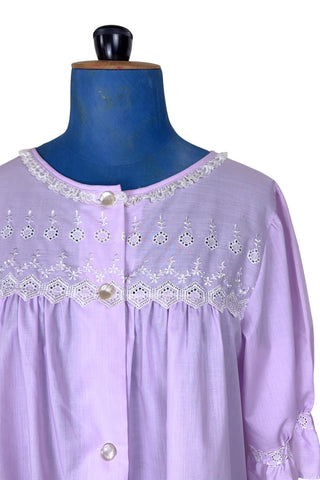Vintage 1960s housecoat in lilac purple cotton blend with delicate white eyelet lace detail across the bust, and trimming the three-quarter length sleeves. The sleeves have gathered ruffle cuffs. The round neckline is trimmed with a tiny white lace ruffle. 

Designed by Adorable Lingerie. Marked size Medium.