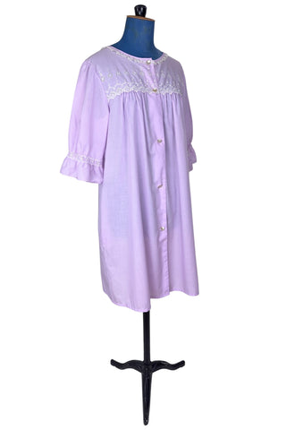 Vintage 1960s housecoat in lilac purple cotton blend with delicate white eyelet lace detail across the bust, and trimming the three-quarter length sleeves. The sleeves have gathered ruffle cuffs. The round neckline is trimmed with a tiny white lace ruffle. 

Designed by Adorable Lingerie. Marked size Medium.