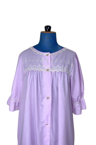 Vintage 1960s housecoat in lilac purple cotton blend with delicate white eyelet lace detail across the bust, and trimming the three-quarter length sleeves. The sleeves have gathered ruffle cuffs. The round neckline is trimmed with a tiny white lace ruffle. 

Designed by Adorable Lingerie. Marked size Medium.