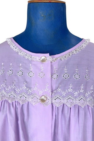 Vintage 1960s housecoat in lilac purple cotton blend with delicate white eyelet lace detail across the bust, and trimming the three-quarter length sleeves. The sleeves have gathered ruffle cuffs. The round neckline is trimmed with a tiny white lace ruffle. 

Designed by Adorable Lingerie. Marked size Medium.