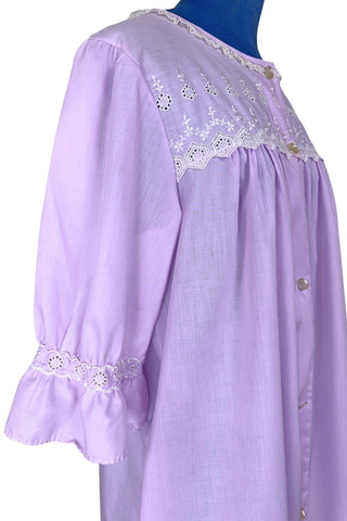 Vintage 1960s housecoat in lilac purple cotton blend with delicate white eyelet lace detail across the bust, and trimming the three-quarter length sleeves. The sleeves have gathered ruffle cuffs. The round neckline is trimmed with a tiny white lace ruffle. 

Designed by Adorable Lingerie. Marked size Medium.