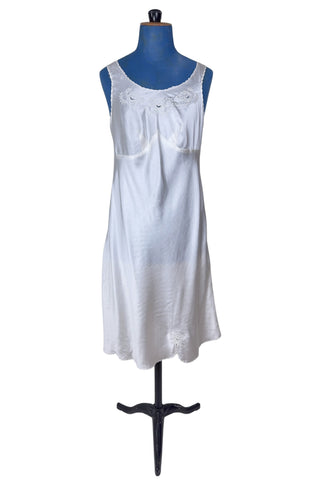 Vintage 1940s nightgown or slip, with cutwork embroidery across the bust, a pointed midriff yoke with vertical bust darts, and scalloped edging around the wide round neckline and hem. The hem has a small kick slit at the left, accented with floral appliqué and embroidery.
