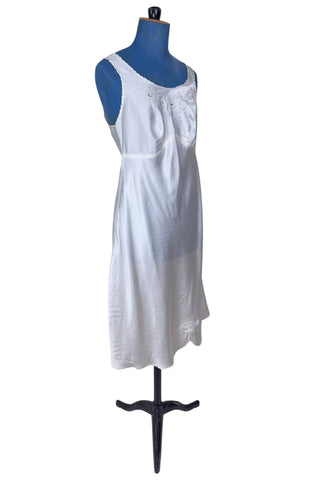 Vintage 1940s nightgown or slip, with cutwork embroidery across the bust, a pointed midriff yoke with vertical bust darts, and scalloped edging around the wide round neckline and hem. The hem has a small kick slit at the left, accented with floral appliqué and embroidery.