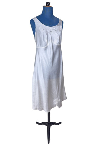 Vintage 1940s nightgown or slip, with cutwork embroidery across the bust, a pointed midriff yoke with vertical bust darts, and scalloped edging around the wide round neckline and hem. The hem has a small kick slit at the left, accented with floral appliqué and embroidery.