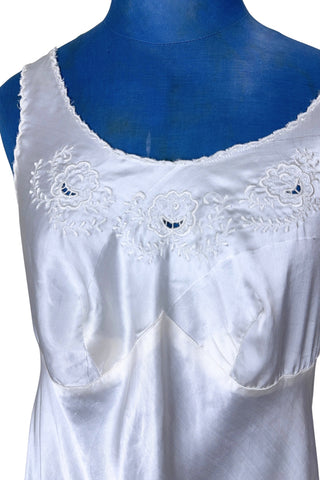 Vintage 1940s nightgown or slip, with cutwork embroidery across the bust, a pointed midriff yoke with vertical bust darts, and scalloped edging around the wide round neckline and hem. The hem has a small kick slit at the left, accented with floral appliqué and embroidery.