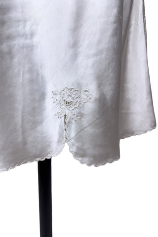 Vintage 1940s nightgown or slip, with cutwork embroidery across the bust, a pointed midriff yoke with vertical bust darts, and scalloped edging around the wide round neckline and hem. The hem has a small kick slit at the left, accented with floral appliqué and embroidery.