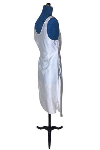 Vintage 1940s nightgown or slip, with cutwork embroidery across the bust, a pointed midriff yoke with vertical bust darts, and scalloped edging around the wide round neckline and hem. The hem has a small kick slit at the left, accented with floral appliqué and embroidery.