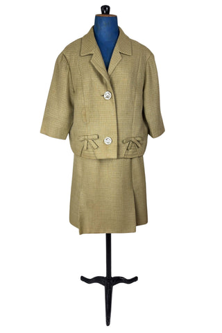 Vintage 1960s skirt suit with oversized jacket and matching skirt. The jacket features three-quarter length sleeves, bow accents at the waist, and closes with two large textured lucite buttons. The skirt has a pleat panel in the front, and closes in the back with a metal zipper.

The jacket and skirt are both lined in caramel brown rayon.

The jacket has a few light stains on the front, which would likely be removed with dry cleaning.