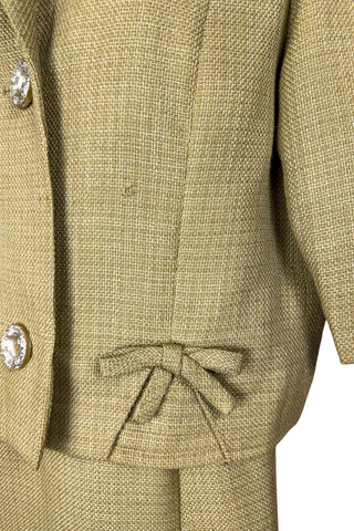 Vintage 1960s skirt suit with oversized jacket and matching skirt. The jacket features three-quarter length sleeves, bow accents at the waist, and closes with two large textured lucite buttons. The skirt has a pleat panel in the front, and closes in the back with a metal zipper.

The jacket and skirt are both lined in caramel brown rayon.

The jacket has a few light stains on the front, which would likely be removed with dry cleaning.