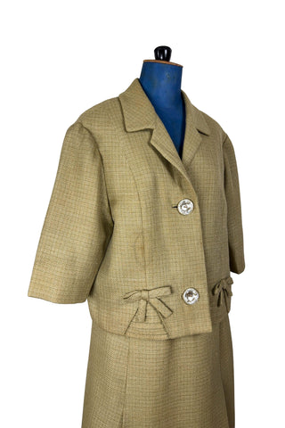 Vintage 1960s skirt suit with oversized jacket and matching skirt. The jacket features three-quarter length sleeves, bow accents at the waist, and closes with two large textured lucite buttons. The skirt has a pleat panel in the front, and closes in the back with a metal zipper.

The jacket and skirt are both lined in caramel brown rayon.

The jacket has a few light stains on the front, which would likely be removed with dry cleaning.