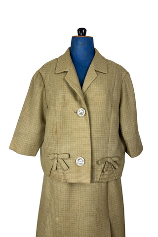 Vintage 1960s skirt suit with oversized jacket and matching skirt. The jacket features three-quarter length sleeves, bow accents at the waist, and closes with two large textured lucite buttons. The skirt has a pleat panel in the front, and closes in the back with a metal zipper.

The jacket and skirt are both lined in caramel brown rayon.

The jacket has a few light stains on the front, which would likely be removed with dry cleaning.