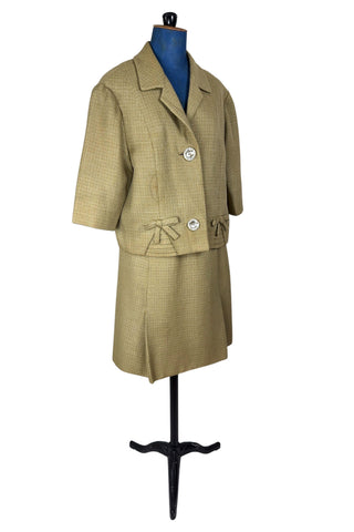 Vintage 1960s skirt suit with oversized jacket and matching skirt. The jacket features three-quarter length sleeves, bow accents at the waist, and closes with two large textured lucite buttons. The skirt has a pleat panel in the front, and closes in the back with a metal zipper.

The jacket and skirt are both lined in caramel brown rayon.

The jacket has a few light stains on the front, which would likely be removed with dry cleaning.